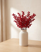 Artificial berry branches standing in a plain off-white vase on a pale oak table; no vase is included