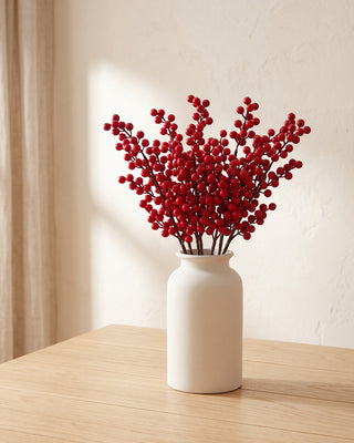Artificial berry branches standing in a plain off-white vase on a pale oak table; no vase is included