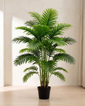 An artificial palm leaf bush with twelve fronds in a plain black nursery pot on pale oak floorboards in a bright room; pot not included