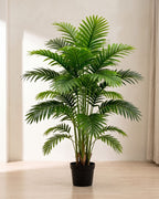An artificial palm leaf bush with twelve fronds in a plain black nursery pot on pale oak floorboards in a bright room; pot not included
