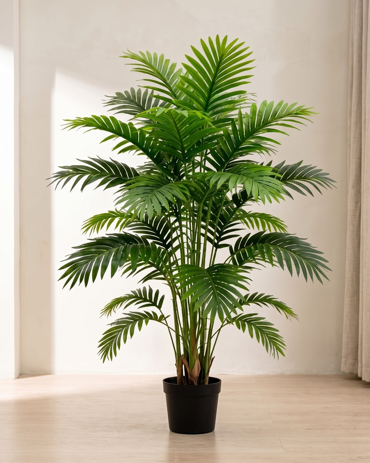 An artificial palm leaf bush with twelve fronds in a plain black nursery pot on pale oak floorboards in a bright room; pot not included