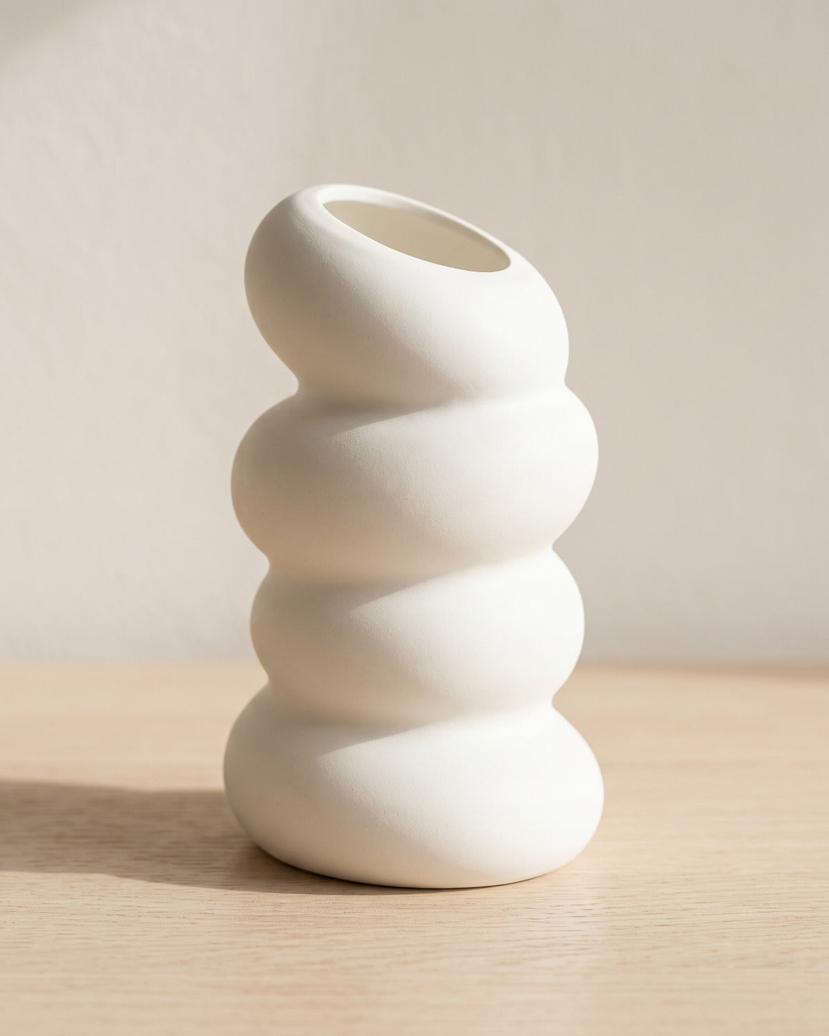 A spiral bud vase in matte white, empty, on a pale oak table