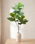 Fiddle leaf artificial tree branch standing in a plain off-white vase on a pale oak table; no vase is included