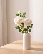 Milky White artificial rose branch standing in a plain off-white vase on a pale oak table; each order is one branch, and no vase is included