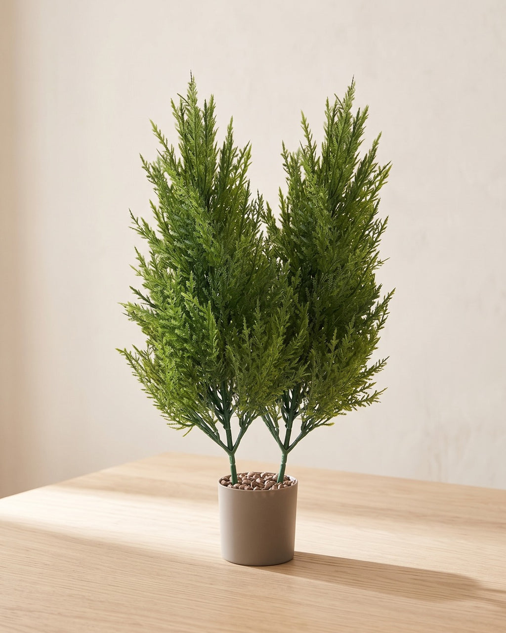 Two artificial pine bundles standing together in a plain nursery pot on a pale oak table; pot not included