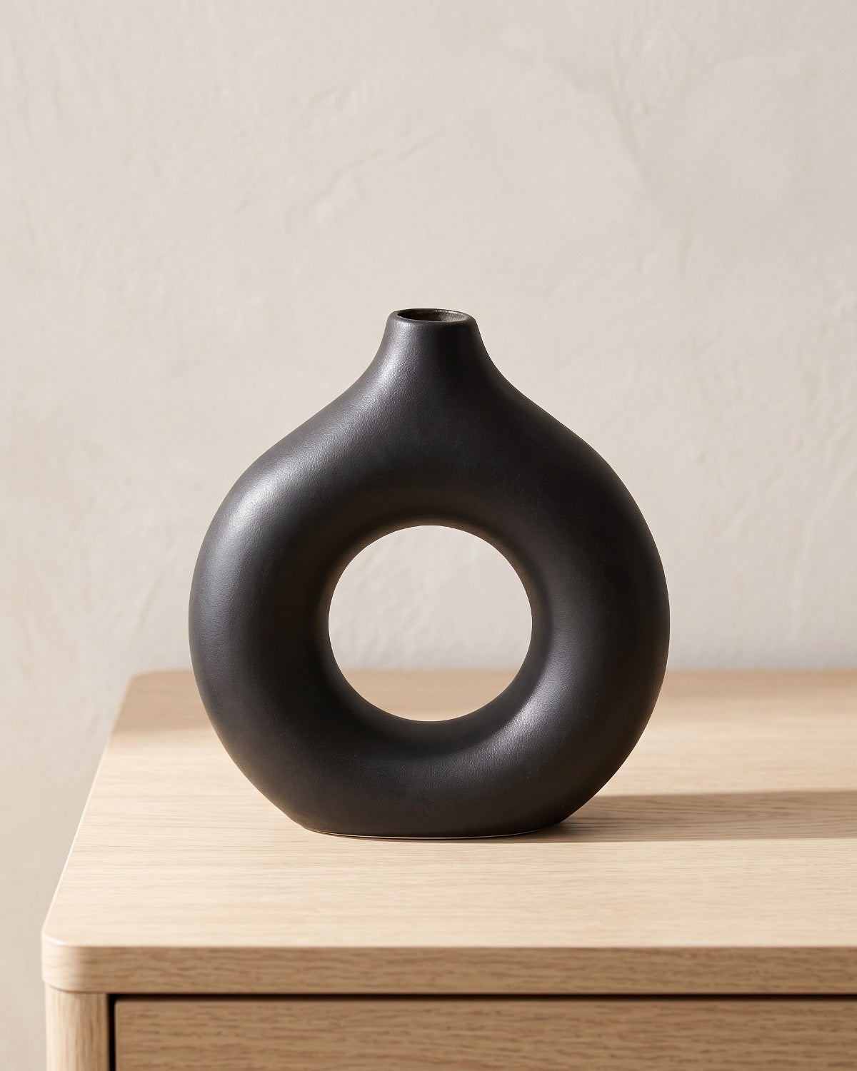 Black donut vase, medium, empty on a pale oak table