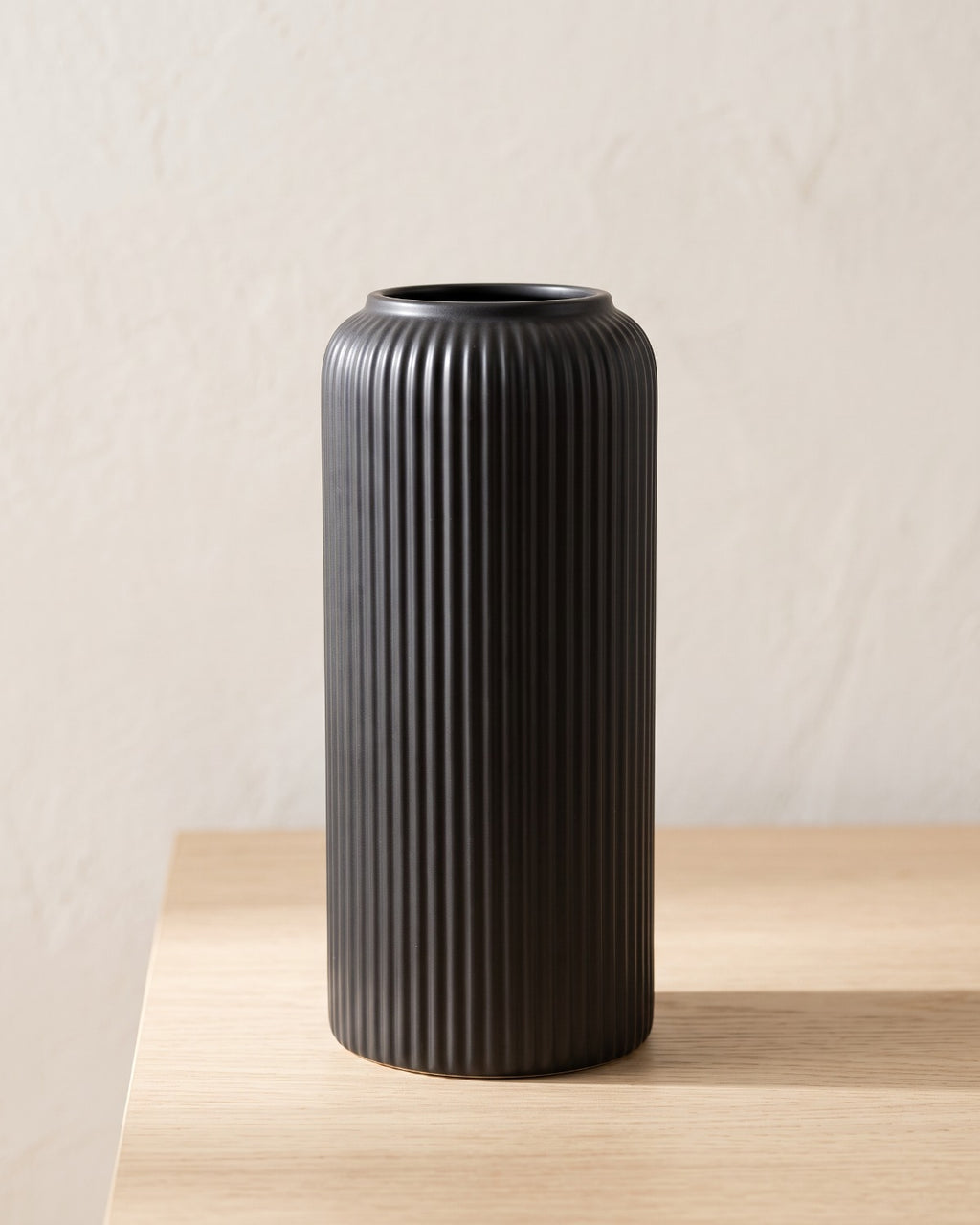 Black striped cylinder vase, empty on a pale oak table