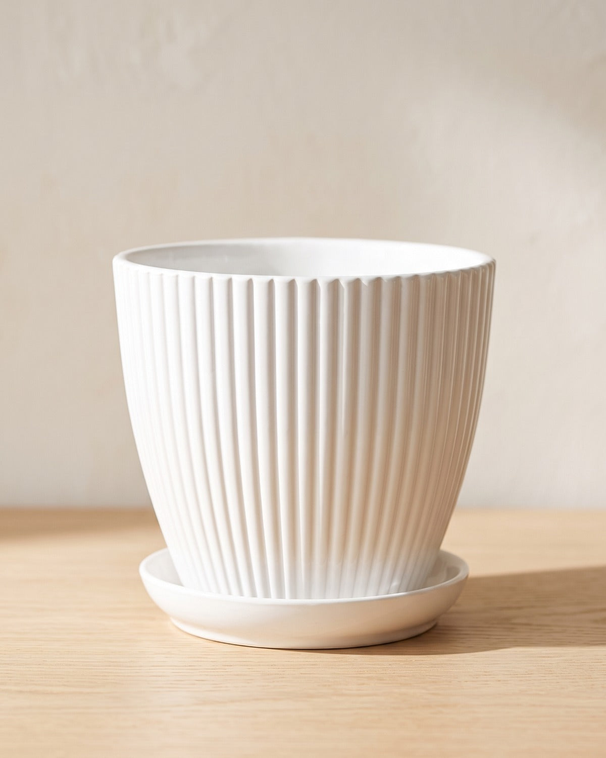 White fluted plant pot and saucer, empty on a pale oak table