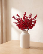 Ten artificial red berry branches in a plain off-white vase on a pale oak table; vase not included