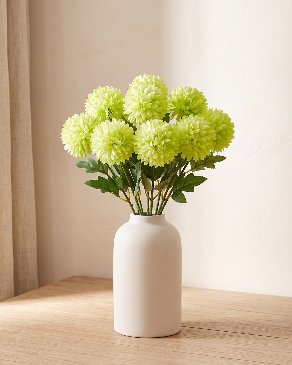 Lime Green artificial pompom chrysanthemums standing in a vase on a pale oak table; no vase is included