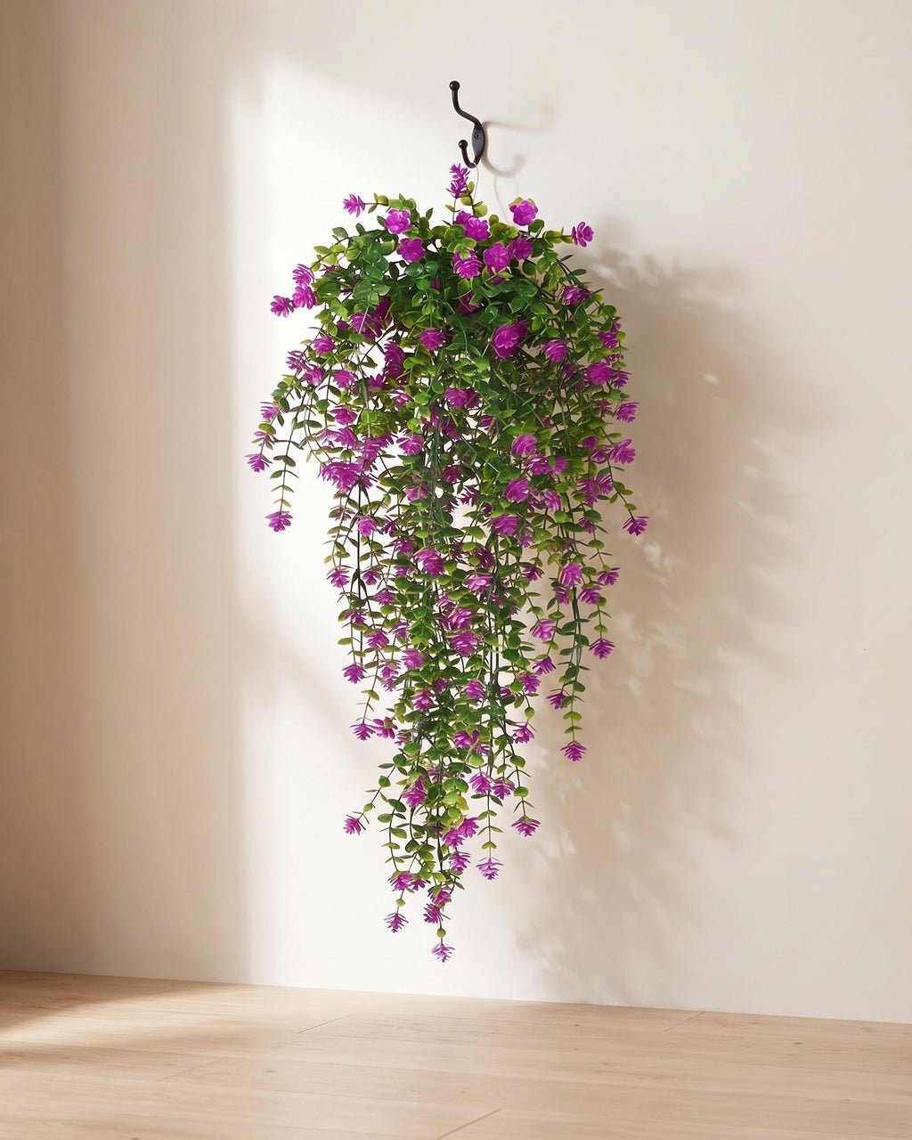 One artificial flowering hanging vine with purple blossoms, on a black iron hook against a warm plaster wall; hook not included