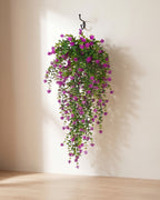 One artificial flowering hanging vine with purple blossoms, on a black iron hook against a warm plaster wall; hook not included