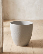 A stone effect plant pot standing empty on pale oak floorboards in a bright room