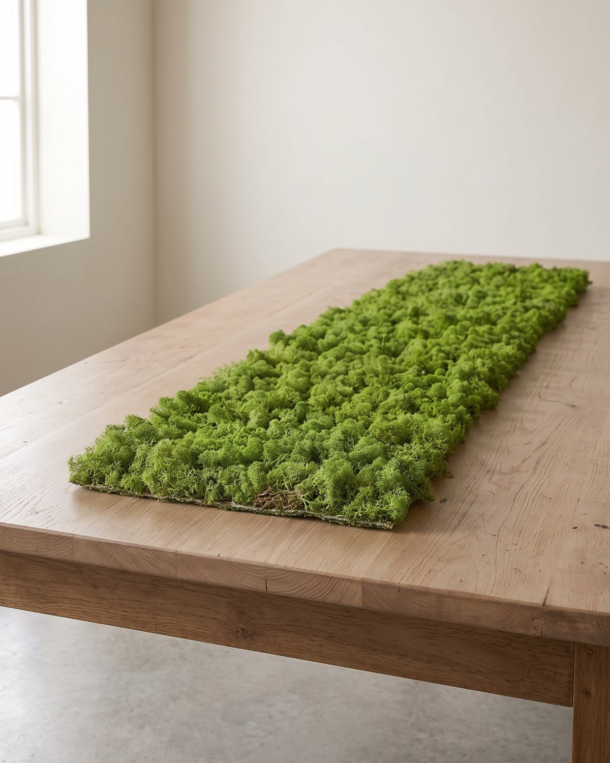 An artificial moss mat lying on a wooden table, twice as long as it is wide; table not included