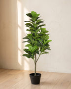 A young artificial fiddle leaf fig tree, leaves on the upper trunk, in its black nursery pot on pale oak floorboards; planter not included