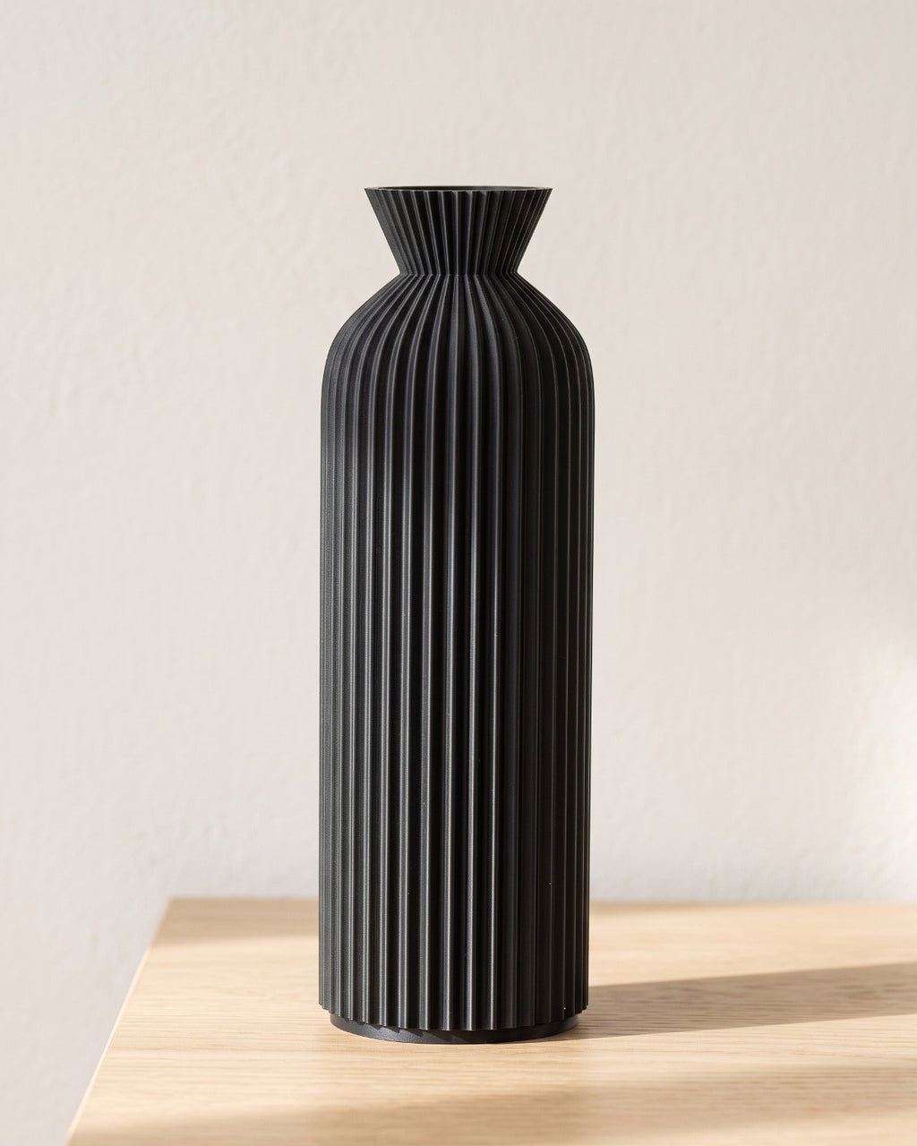 Black ribbed bottle vase, large, empty on a pale oak table