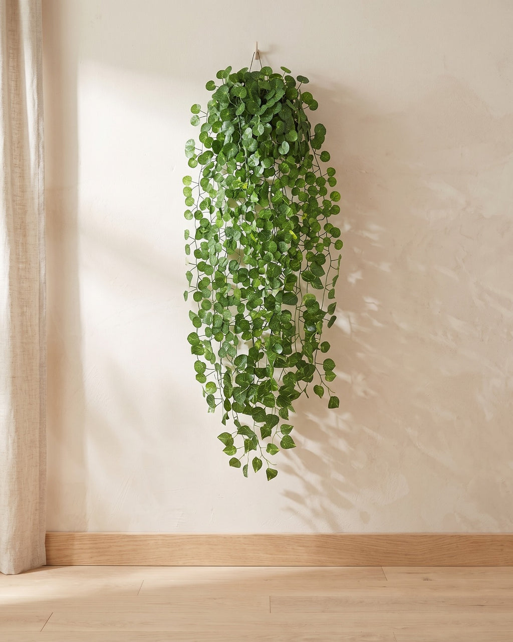 Rounded leaf artificial ivy garland hanging from a simple hook on an off-white plaster wall, its full drop clear of the floor