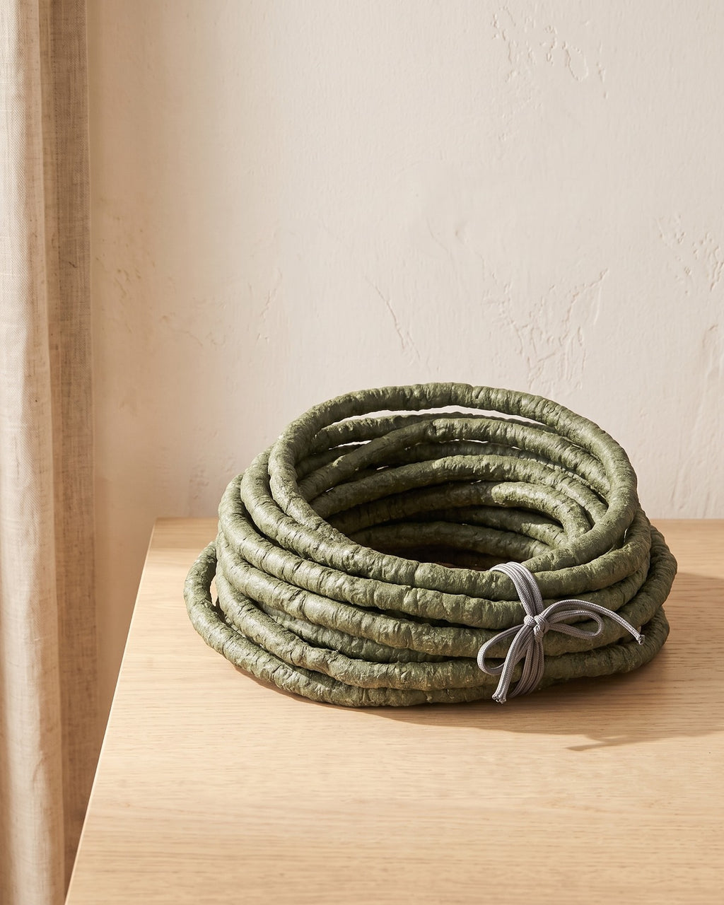 A coil of green artificial jungle vine at its 13 ft length, on a pale oak table