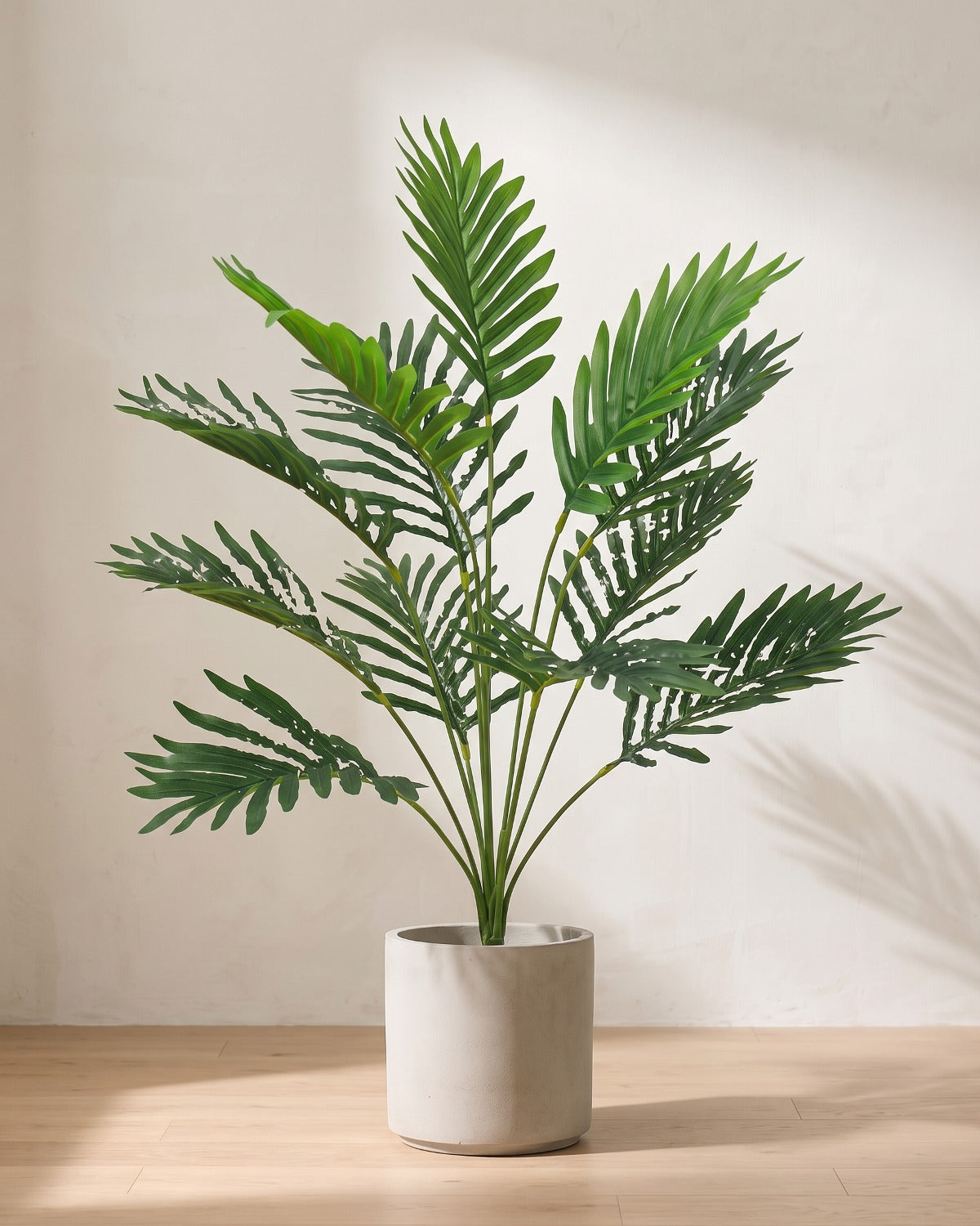 An artificial areca palm with twelve fronds, the smallest of the three, in a plain stone pot on an oak floor; pot not included