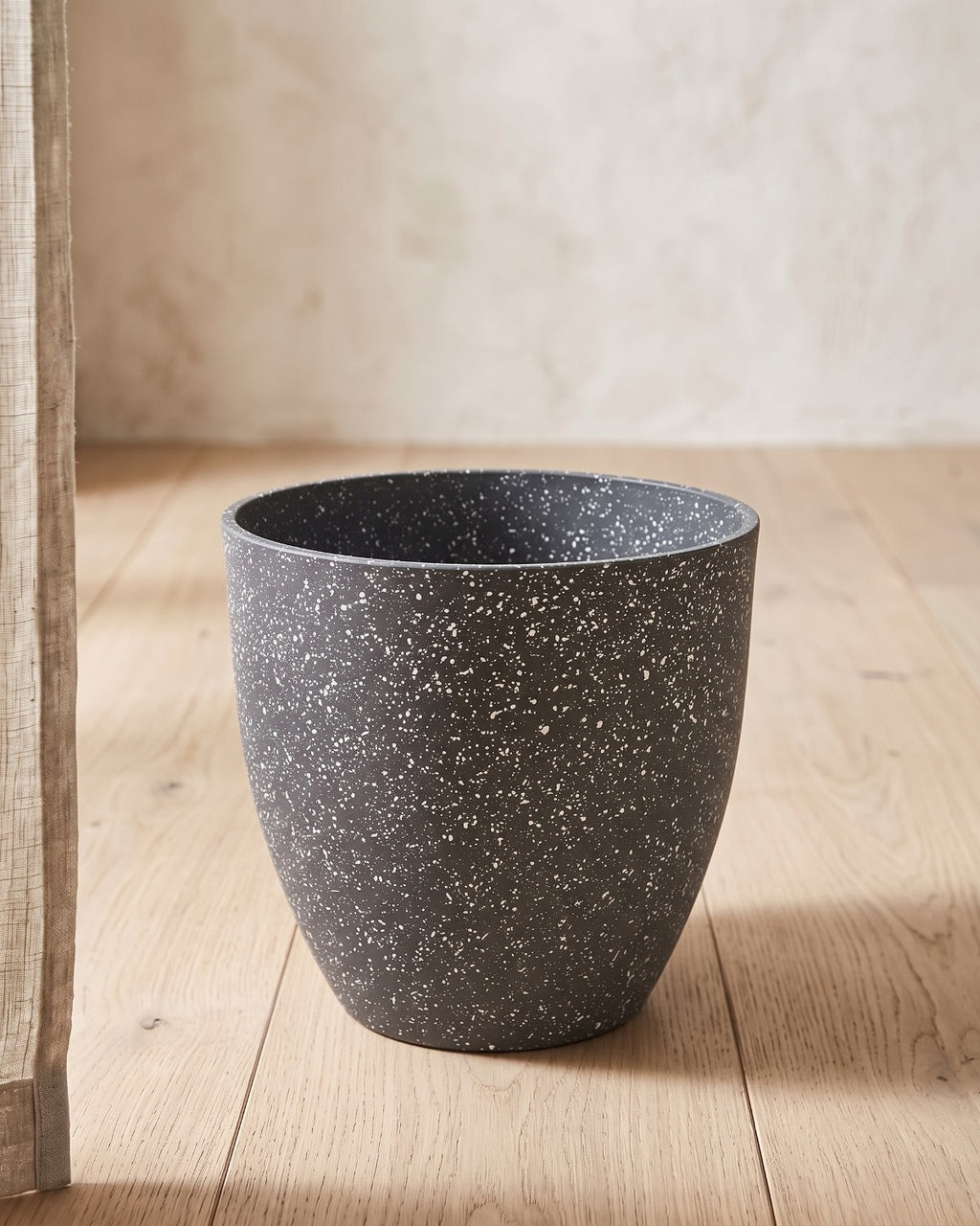 Charcoal stone effect plant pot standing empty on pale oak floorboards against an off-white plaster wall