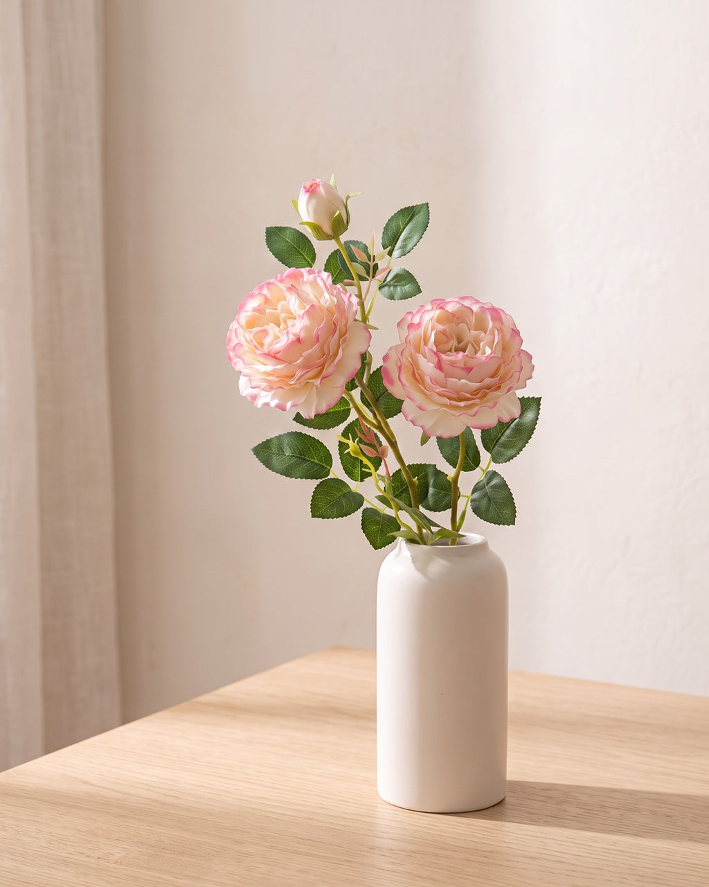 Light Pink artificial rose branch standing in a plain off-white vase on a pale oak table; each order is one branch, and no vase is included