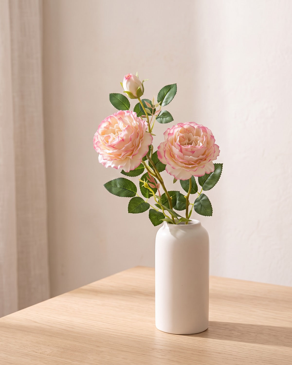 Light Pink artificial rose branch standing in a plain off-white vase on a pale oak table; each order is one branch, and no vase is included