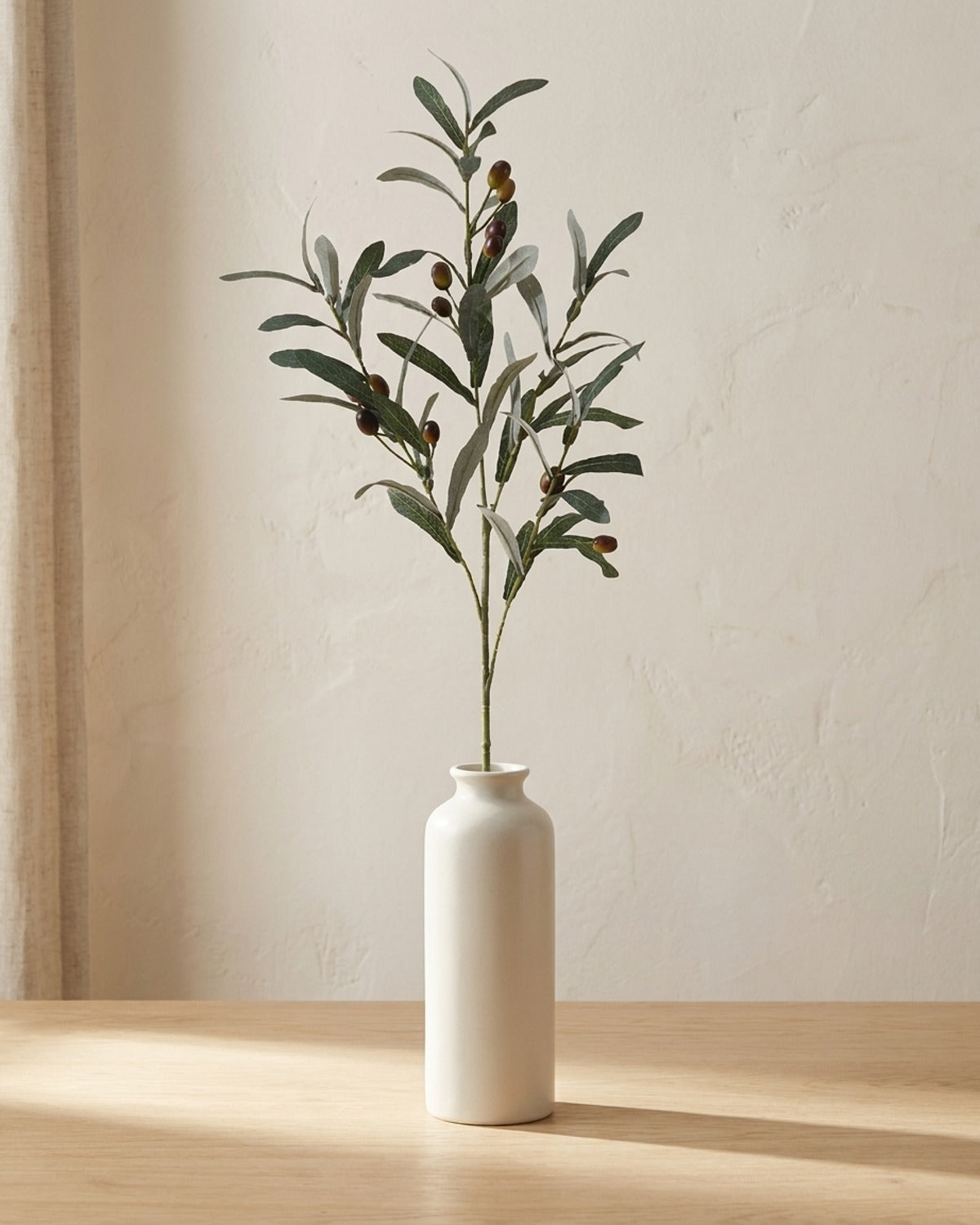 Artificial olive branch in a plain off-white bud vase on a pale oak tabletop, vase not included