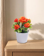 A small artificial flowering pot with orange blooms, in the white pot it comes in, on a pale oak table