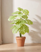 Artificial monstera bush with deeply split leaves in a light pale green, in a plain terracotta pot; pot not included
