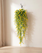 One artificial flowering hanging vine with yellow blossoms, on a black iron hook against a warm plaster wall; hook not included
