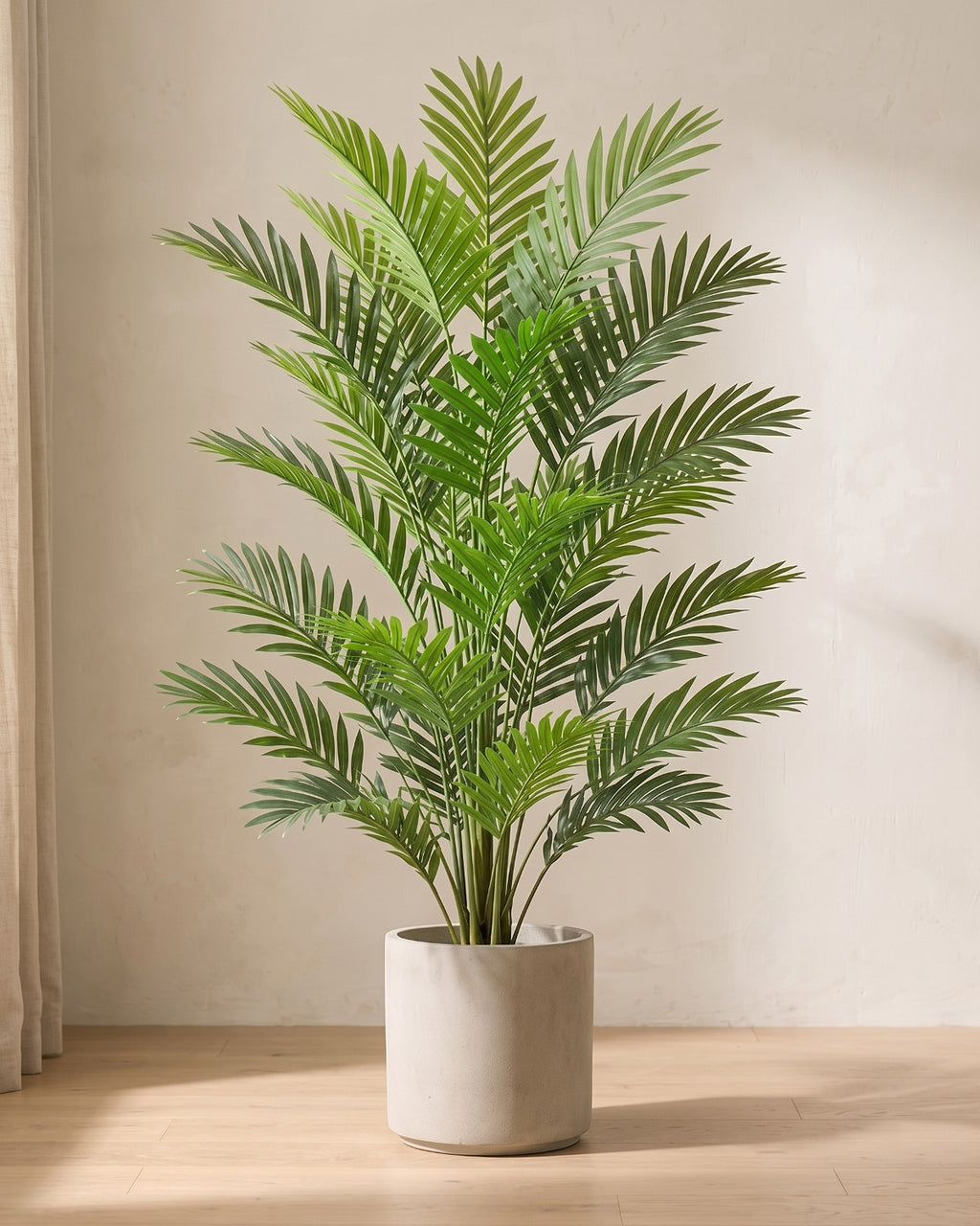 An artificial areca palm with twenty-four fronds, the fullest of the three, in a plain stone pot on an oak floor; pot not included
