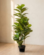 An artificial fiddle leaf fig tree, leaves along most of the trunk, in its black nursery pot on pale oak floorboards; planter not included