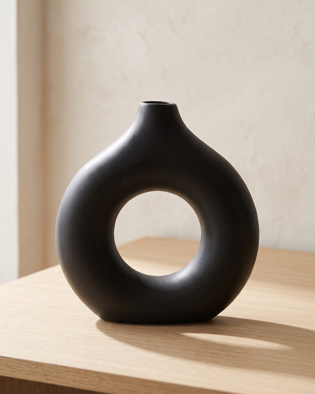Black donut vase, large, empty on a pale oak table