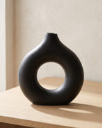 Black donut vase, large, empty on a pale oak table
