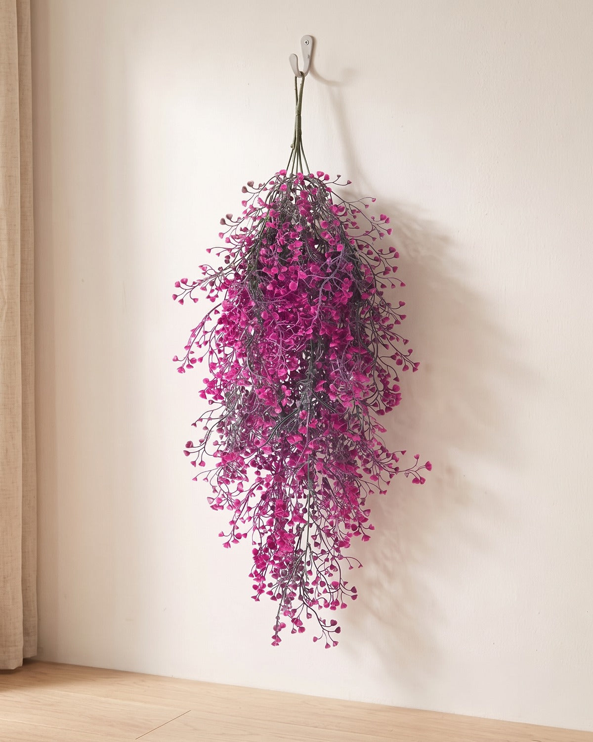 Magenta artificial wisteria vine hanging from a simple hook on an off-white plaster wall, its full drop clear of the floor