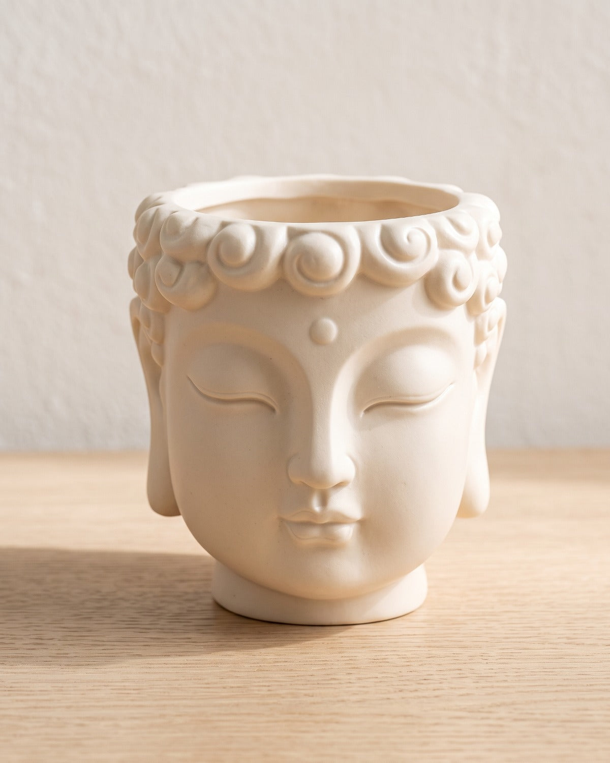 Cream Buddha head planter, empty on a pale oak table