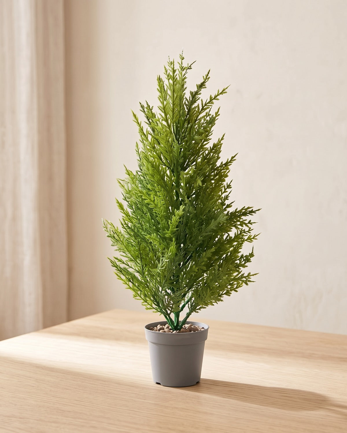 One artificial pine bundle standing in a plain nursery pot on a pale oak table; pot not included