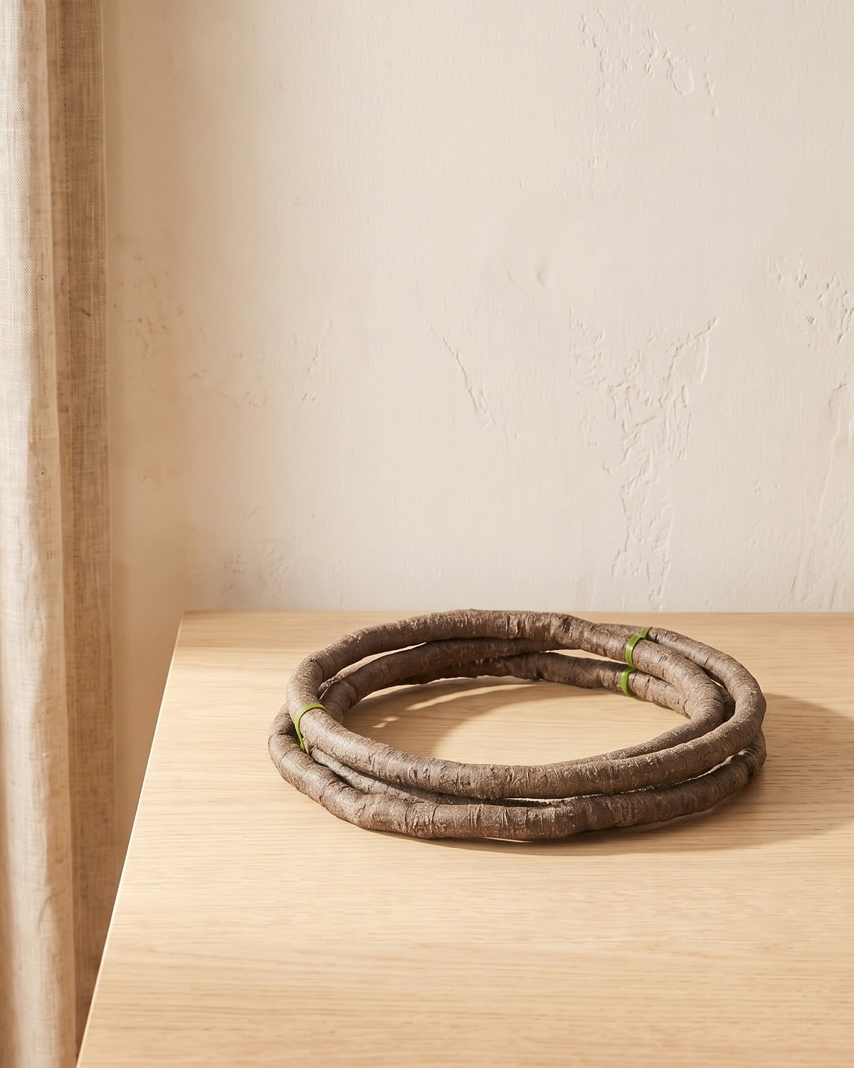 A small coil of brown bark-textured artificial jungle vine at its 3.3 ft length, on a pale oak table