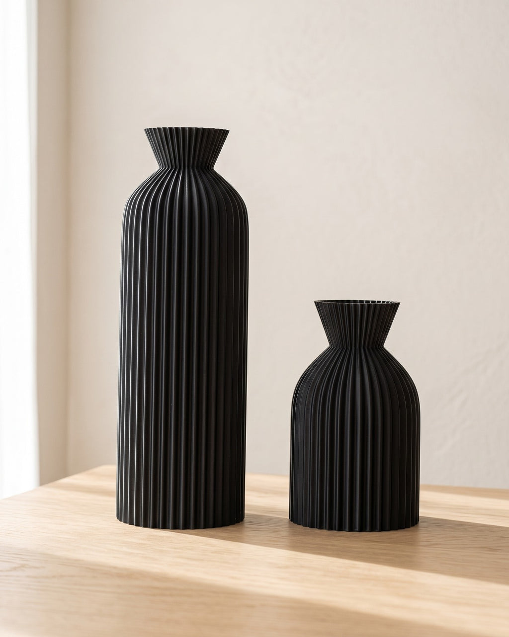Black ribbed bottle vases, both sizes, empty on a pale oak table
