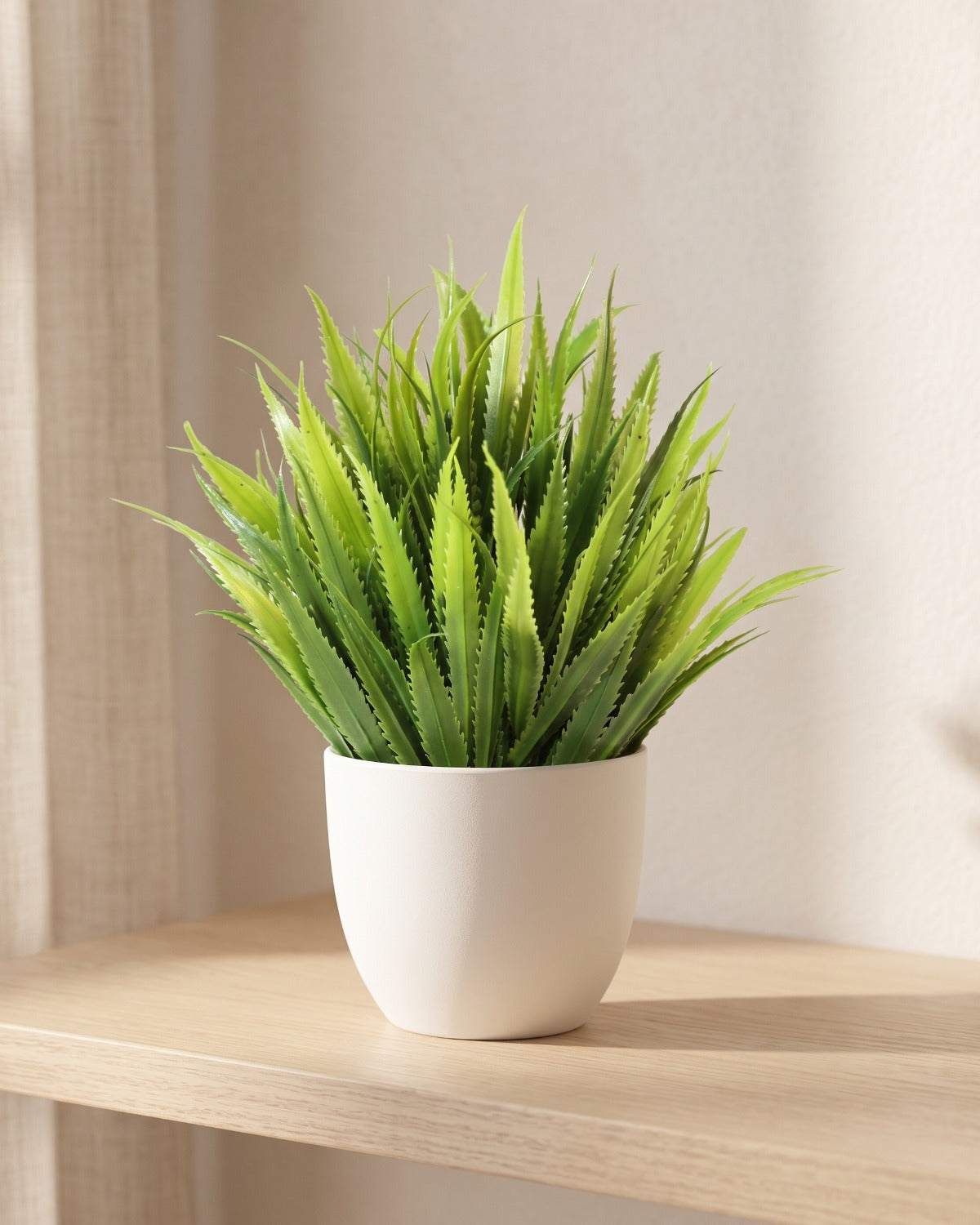 Grass style mini artificial potted plant in a plain white pot on a pale oak table