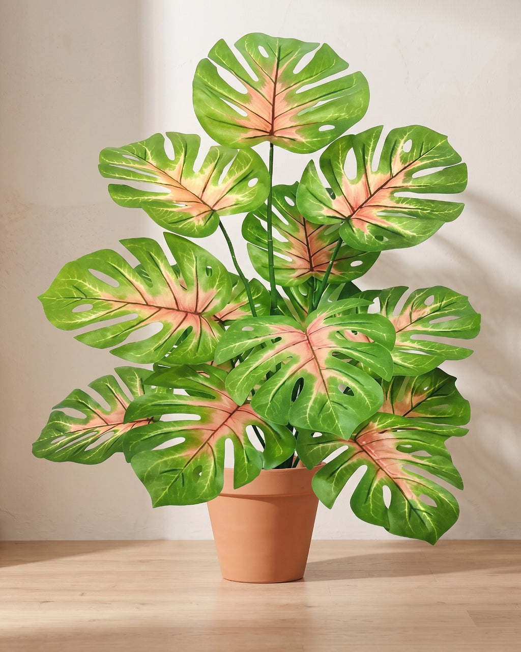 Artificial monstera bush with split leaves veined in pink over mid green, in a plain terracotta pot; pot not included