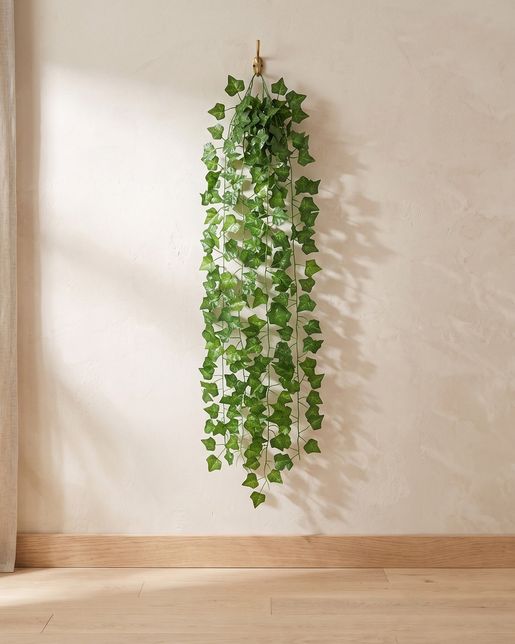 Classic ivy leaf artificial ivy garland hanging from a simple hook on an off-white plaster wall, its full drop clear of the floor