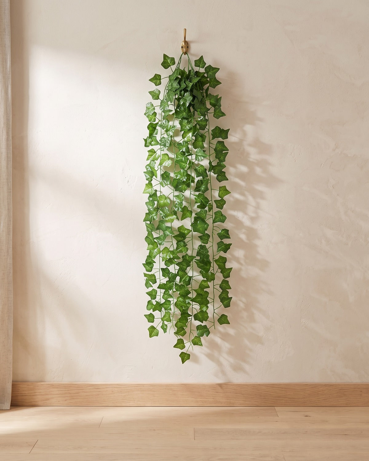 Classic ivy leaf artificial ivy garland hanging from a simple hook on an off-white plaster wall, its full drop clear of the floor