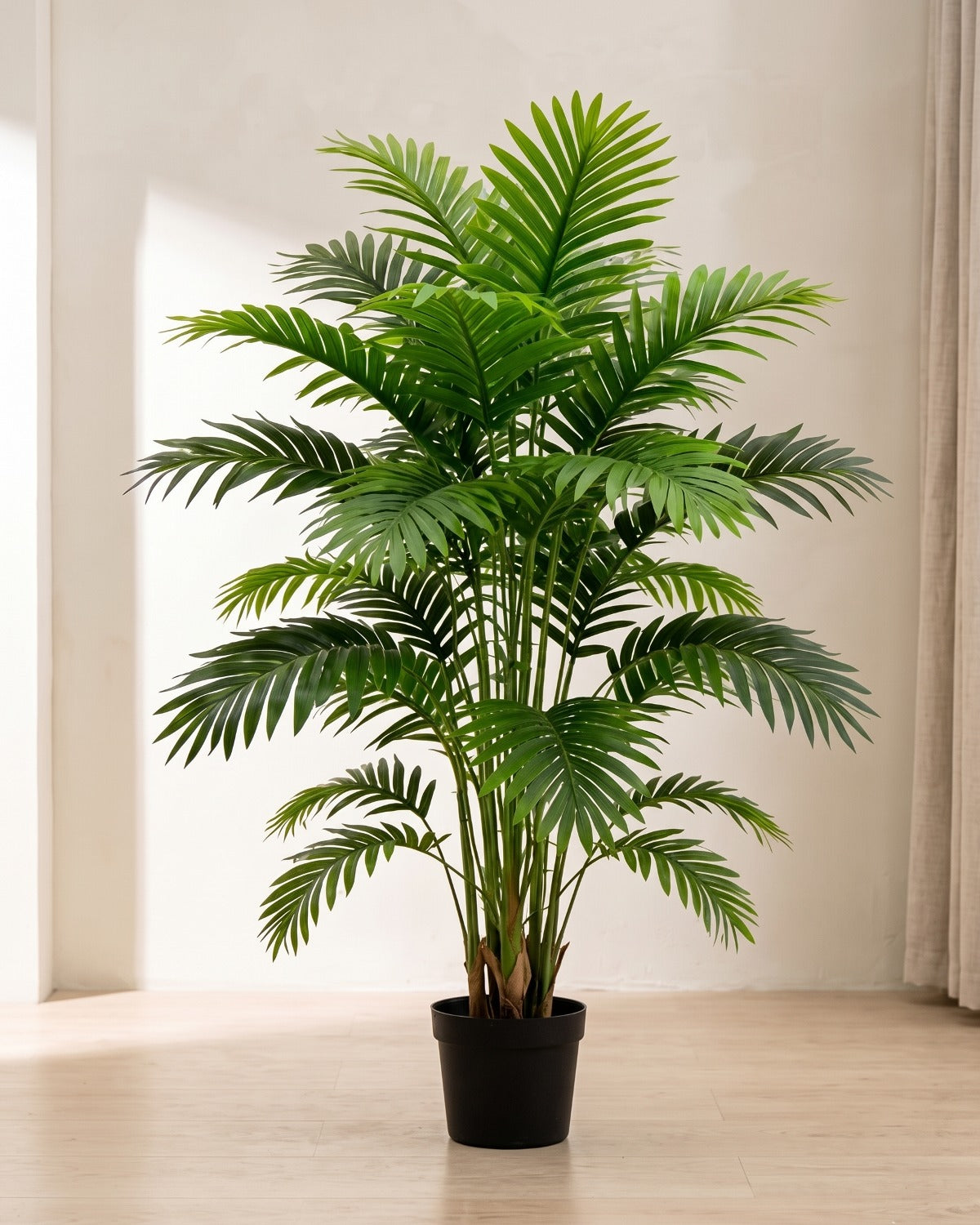 An artificial palm leaf bush with twenty-one fronds in a plain black nursery pot on pale oak floorboards in a bright room; pot not included