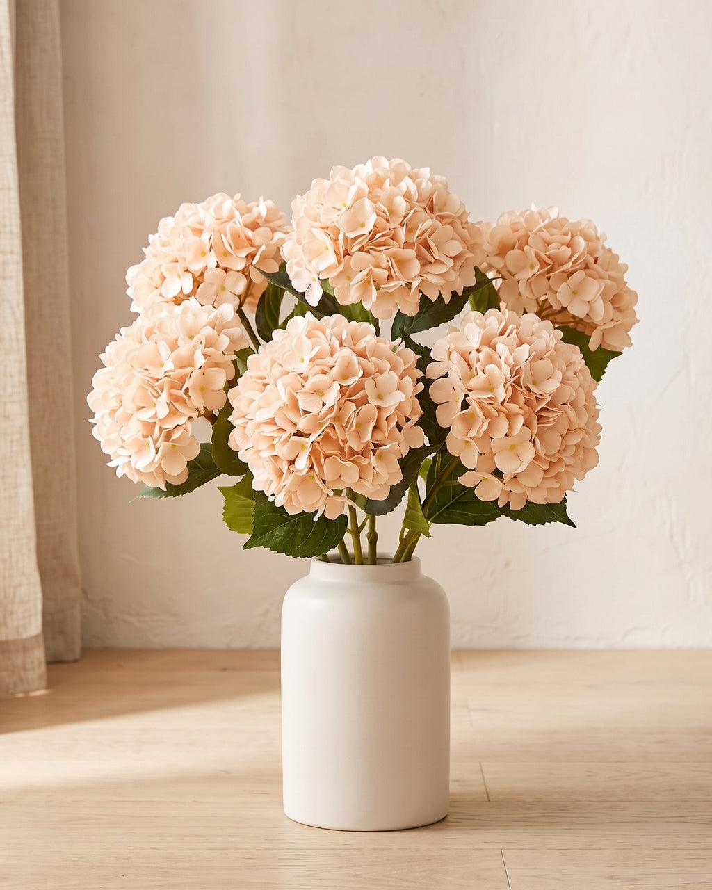 Champagne artificial hydrangea flowers standing in a plain off-white vase on a pale oak table; no vase is included