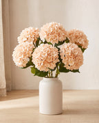 Champagne artificial hydrangea flowers standing in a plain off-white vase on a pale oak table; no vase is included