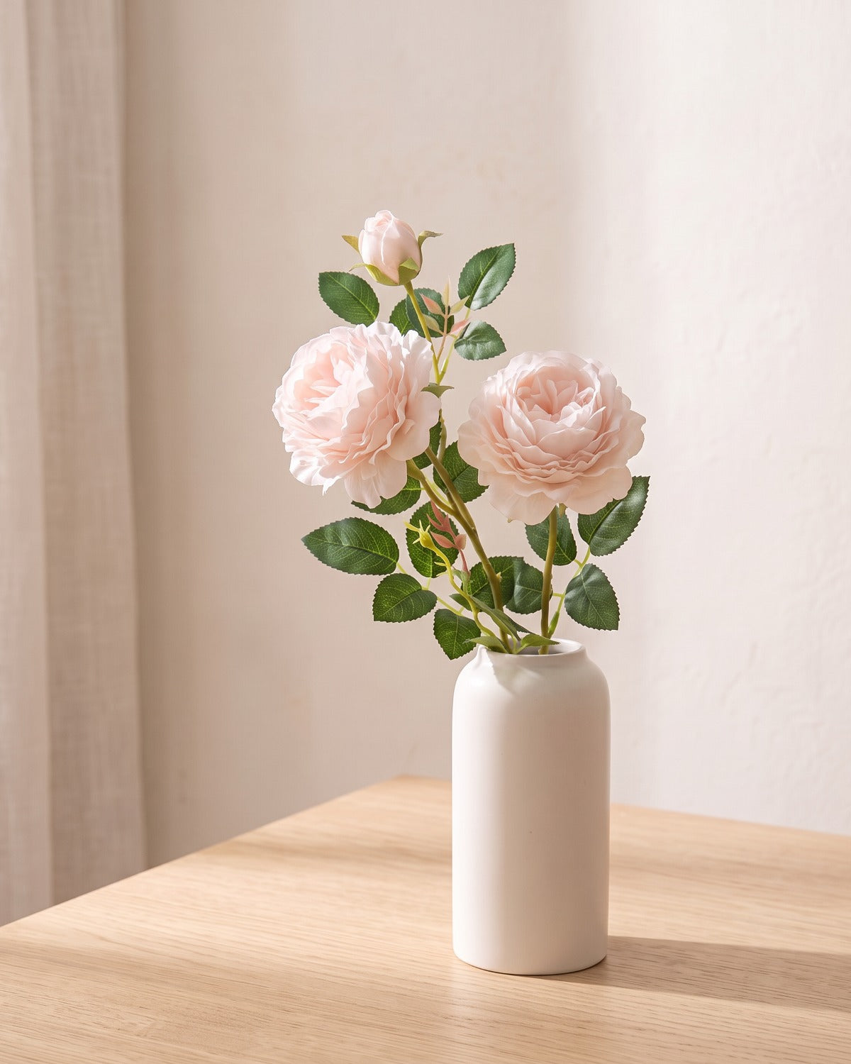 Milk Pink artificial rose branch standing in a plain off-white vase on a pale oak table; each order is one branch, and no vase is included