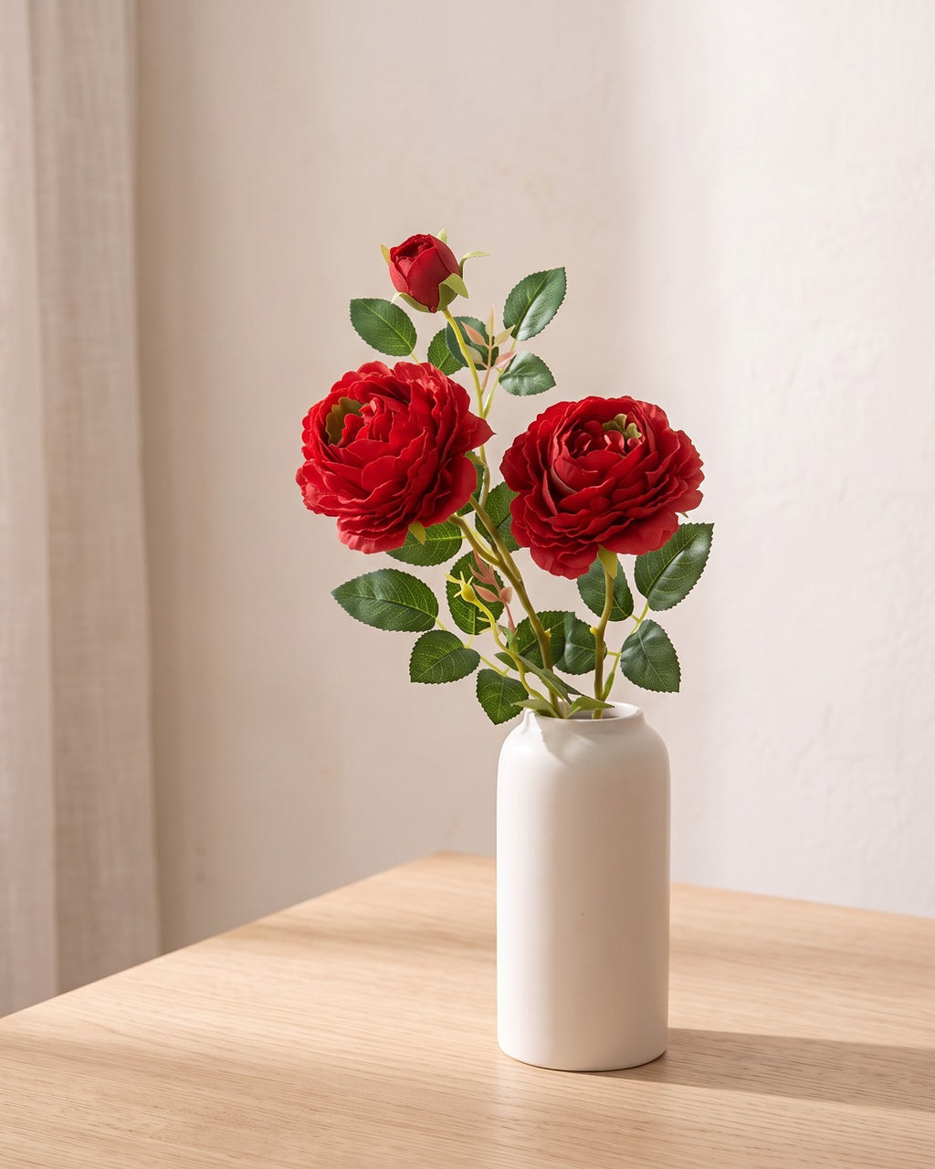 Red artificial rose branch standing in a plain off-white vase on a pale oak table; each order is one branch, and no vase is included