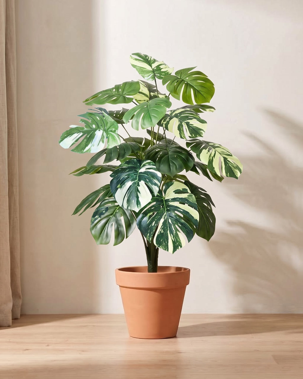 Artificial monstera bush with split leaves patched in cream and pale green, in a plain terracotta pot; pot not included