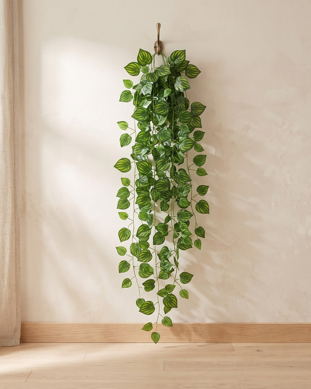 Marbled leaf artificial ivy garland hanging from a simple hook on an off-white plaster wall, its full drop clear of the floor